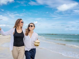 Beautiful young lesbian couple with white shirts with fresh coconuts in their hands walks on a tropical paradise beach, wedding, honeymoon, travel, vacation concept