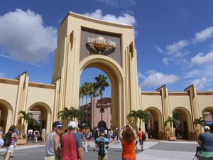 Entrance to Universal Orlando. People are walking and taking picture of the sign above the entrance arch