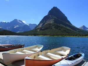 two rowboats, a kayak, and two canoes on a short pier with a mountain in the distance