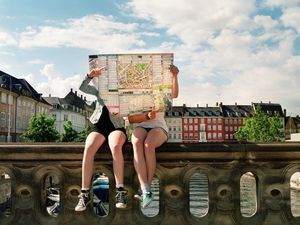 Two teenagers sitting on a ledge using a paper map