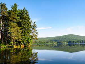 calm lake surface with reflections of surrounding pine trees and hills