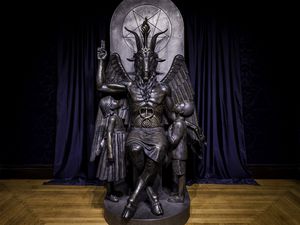 Dark bronze sculpture of a seated Baphomet (a goat-headed deity) with two bronze children looking up at Baphoment