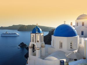 Blue domed churches at sunset, Oia, Santorini with a cruise ship in the background