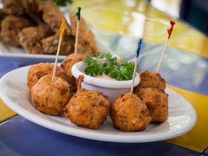 8 conch fritters in a circle on a plate with a small cup of sauce in the middle. Every other fritter has a toothpick in it