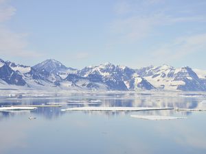 Snow covered mountains in Greenland and sea ice photographed on a clear day reflected in still water.