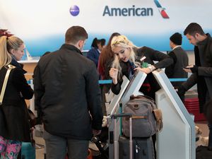 traveling couple looking at an airport kiosk while a blonde American airlines employee uses the kiosk
