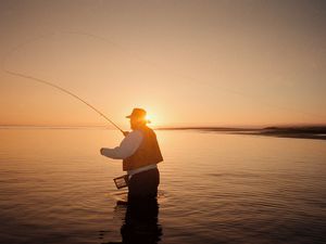 Person fly fishing for striped bass at sunset