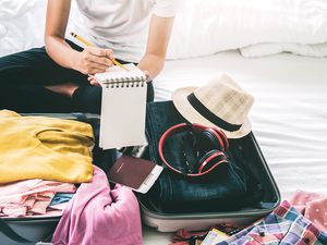Midsection Of Woman Packing Luggage While Sitting On Bed At Home