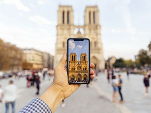Tourist taking picture of Notre Dame cathedral with smart phone, personal perspective view