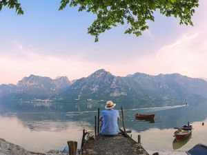 back view of man sitting on jetty at Lake Idro in Lombardy, Italy at morning twilight