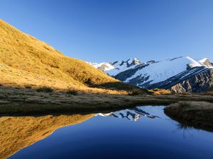 lake with reflection of blue sky, snowy mountains and grassy hill