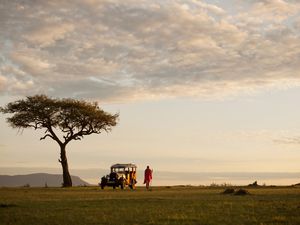 Maasai tribesman stands by a classic safari Jeep, Kenya