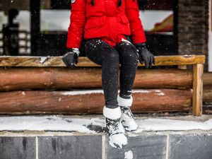 Person sitting on a wooden bench with boots covered in snow
