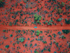 Aerial shot of a blue car driving along a red dirt road