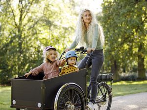 Mother cycling with two children in electric cargo bicycle