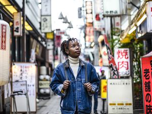 Black woman in her 20s with braided hair and glasses looking up at signs on a Tokyo street