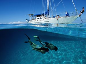 Two snorkelers dive under the water with a yacht in the background