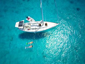 Aerial view of couple snorkeling next to a luxury sailboat