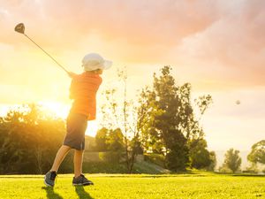Young Boy Golfer Teeing Off During Sunset