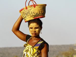 Portrait of a Malagasy woman in a traditional face mask holding a basket on her head