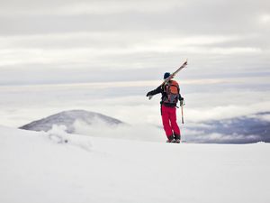 A skier stands on a ridge with his skies slung over his shoulder