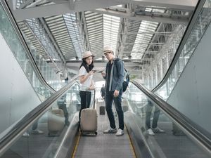 Young Asian couple with luggage down the escalator