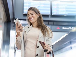 Businesswoman with passport using cell phone in airport