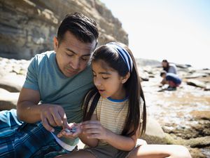 Father and daughter looking at rocks on sunny beach