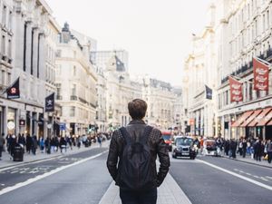 A solo traveler walks down a busy street wearing a backpack