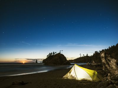 Illuminated tent on sea shore against blue sky at dusk