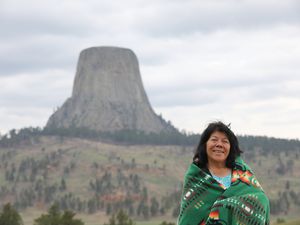 An Indigenous woman wrapped in a blanket smiling in front of Devil's Tower in Wyoming