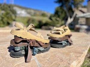 Three pairs of Chaco hiking sandals stacked outdoors on a stone surface