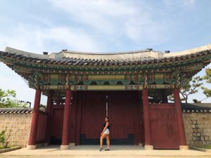 Sherri (a light skinned black woman wearing shorts and a tanktop) posing in front of a red gate at Gyeongbokgung palace in Seoul, South Korea