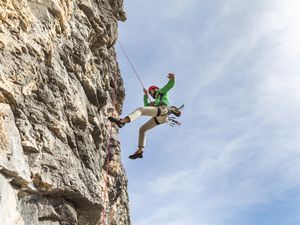 man in a green shirt and red helmet abseiling in the Dolomites mountains