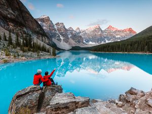 two people in red coats sitting on a rock looking at an alpine lake in Banff National Park