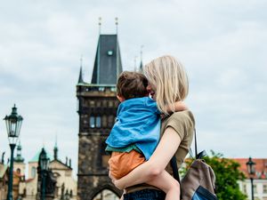 Blonder Mother holding her brunette son in front of Charles bridge in Prague, Czech Republic. 