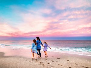 Mother and two children walk on the beach during a vibrant colorful sunset