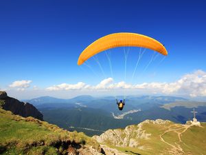 yellow paraglider against blue sky with hills and clouds