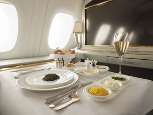 Caviar, and a glass of champagne on a first class Emirates tray table with a basket of bread and a variety of garnishes