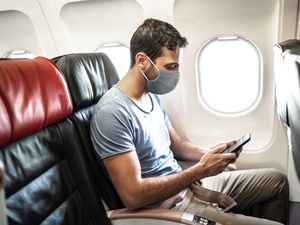 Side view of a man wearing face mask in an airplane using cellphone