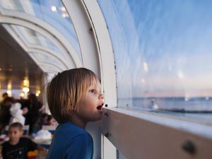 Side view of girl looking through window while traveling in cruise ship