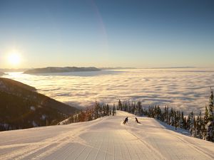 Silhouette of couple skiing above clouds