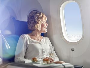 Smiling woman drinking champagne, traveling first class, looking out airplane window