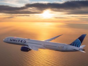 A United Airlines airplane flying over water at sunset 