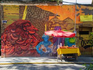 A fruit cart parked in front of a wall with a large mural on it