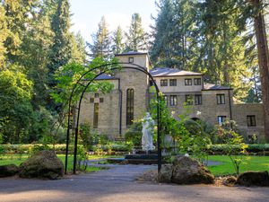 stone building in a park surrounded by trees with a white statue out from