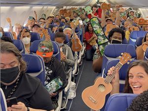 Group of pepole sitting on an airplane holding up ukuleles and smiling