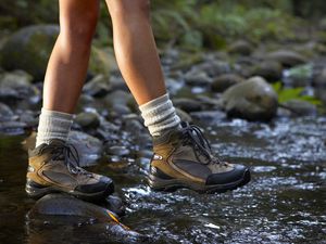 woman crossing stream wearing hiking boots