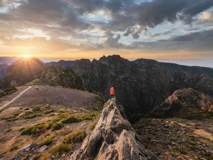 Woman standing on top of a rock admiring sunset at Pico do Arieiro, Madeira, Portugal