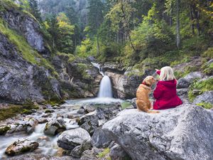 Woman with Golden Retriever dog enjoys the silence at the waterfall in the Alps